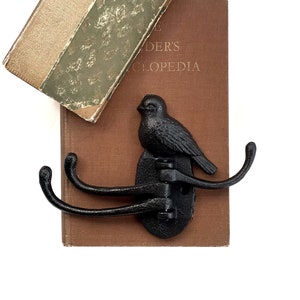 May include: Black cast iron bird hook with three hooks. The hook is mounted on a brown book with the text "Reader's Encyclopedia".