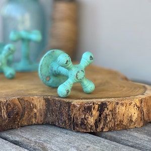 May include: A set of three turquoise blue metal hooks shaped like vintage water faucets. The hooks are mounted on a wooden slice.
