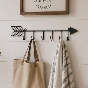 May include: A wooden bench with two wicker baskets and a central drawer, topped with a tall ceramic vase, a striped pillow, a wire basket with books, and black rubber boots. A wall-mounted arrow hook rack holds a beige tote and a striped throw.