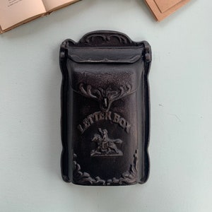 May include: A black cast iron mailbox with the words "LETTER BOX" embossed on the front. The mailbox has a decorative design with a floral motif and a small figure of a person riding a horse.