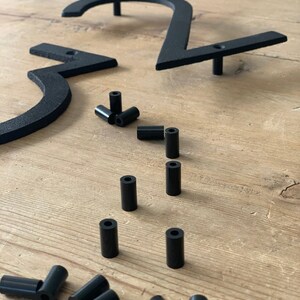 May include: Black metal house numbers, including the numbers 2 and 3, with mounting hardware. The numbers are in a modern font and are shown with several black cylindrical spacers. The numbers are designed for outdoor use.