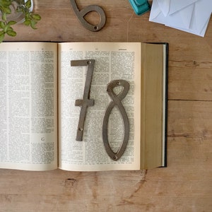 May include: An open book with the numbers 6, 7, and 8 made of metal. The numbers are placed on the pages of the book. A stapler and white envelopes are on the wooden surface.