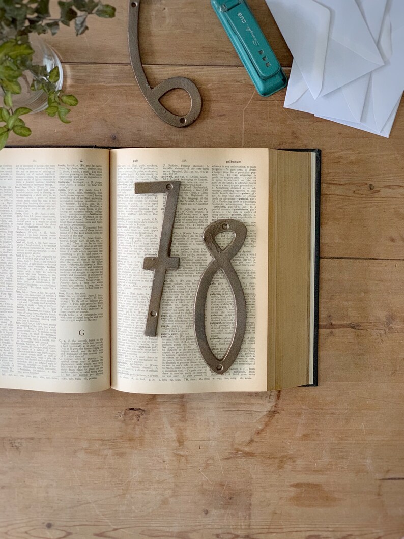 May include: An open book with the numbers 6, 7, and 8 made of metal. The numbers are placed on the pages of the book. A stapler and white envelopes are on the wooden surface.