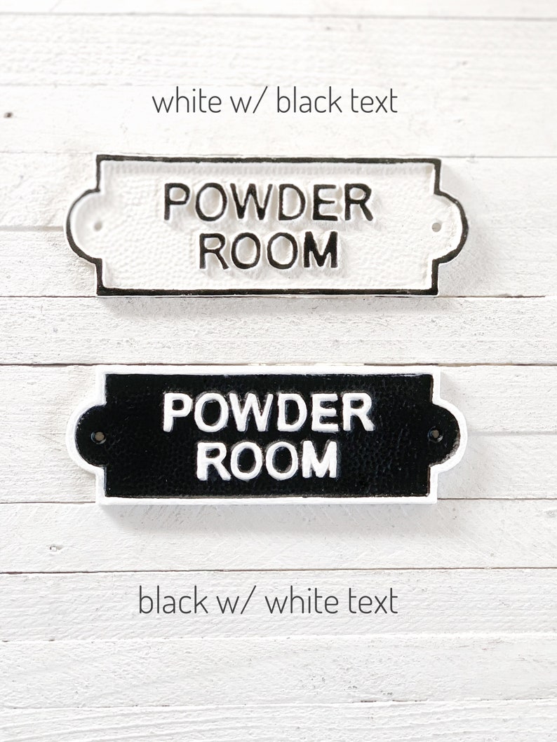 Puede incluir: Dos letreros de hierro fundido que dicen "Powder Room" en blanco y negro. El letrero superior es blanco con texto negro y el letrero inferior es negro con texto blanco.