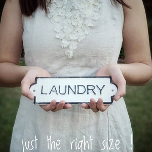 Puede incluir: Una persona con un vestido blanco de lino con un adorno floral blanco sostiene un cartel blanco con letras negras que dice "LAUNDRY". El texto "just the right size!" est&aacute; escrito en blanco en la parte inferior de la imagen.