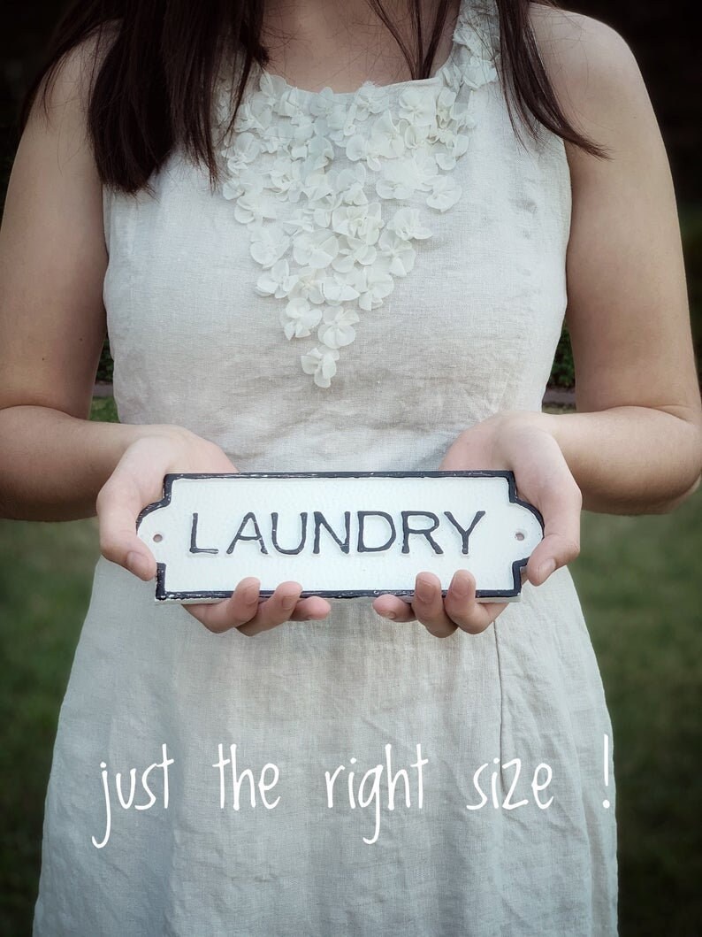 Puede incluir: Una persona con un vestido blanco de lino con un adorno floral blanco sostiene un cartel blanco con letras negras que dice "LAUNDRY". El texto "just the right size!" est&aacute; escrito en blanco en la parte inferior de la imagen.