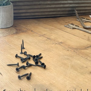 Puede incluir: Primer plano de tornillos negros sobre una superficie de madera. El texto "#mounting hardware included" est&aacute; escrito debajo de los tornillos.