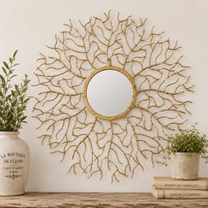 May include: A circular wall mirror featuring a gold-toned frame with an intricate, branching coral-like design extending outward. The central mirror is round with a smooth, reflective surface, surrounded by thin, metallic, twig-like structures.