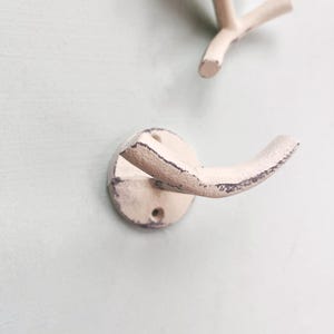 May include: A white metal hook with a distressed finish. The hook is mounted on a light blue wall.