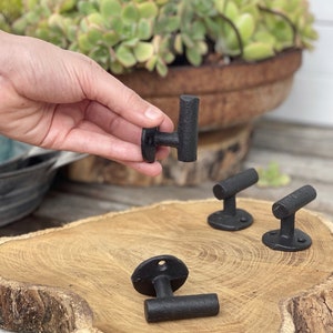 May include: Three black metal hooks with a rounded rectangular shape. The hooks are mounted on a round wooden surface.