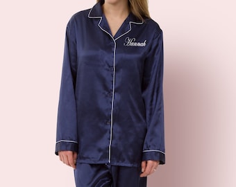 May include: Navy blue satin pajamas with long sleeves and a collared top. The top has a white button closure and a white embroidered name "Hannah" on the left chest.