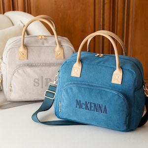 May include: Two corduroy bags with tan handles and straps. One is light gray with the initials "SP" embroidered on the front. The other is blue with the name "McKenna" embroidered on the front. Both have gold zippers.