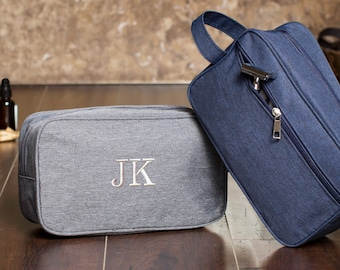 May include: Two toiletry bags, one gray with the initials "JK" embroidered on it and one blue. Both bags have a zipper closure.
