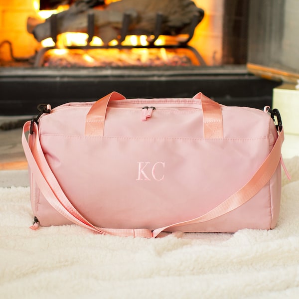 May include: A pink duffel bag with a long strap and the initials "KC" embroidered on the front.