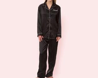 May include: Black satin pajamas with long sleeves and a button-up top. The top has a white piping detail and the name "Hannah" embroidered on the chest.