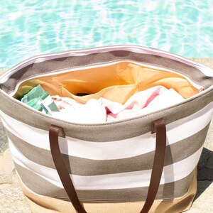 Puede incluir: Una bolsa de lona a rayas con asas de cuero marr&oacute;n. La bolsa est&aacute; abierta y llena de toallas y otros art&iacute;culos esenciales para la playa.