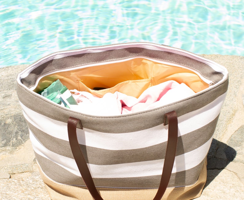 Puede incluir: Una bolsa de lona a rayas con asas de cuero marr&oacute;n. La bolsa est&aacute; abierta y llena de toallas y otros art&iacute;culos esenciales para la playa.