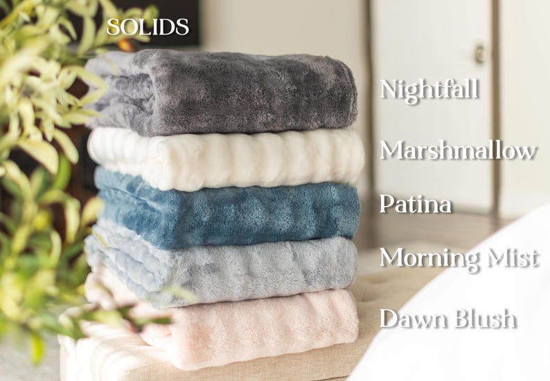 May include: A stack of six plush blankets in various solid colors. The colors include Nightfall, Marshmallow, Patina, Morning Mist, and Dawn Blush. The blankets are soft and fluffy, perfect for adding warmth and comfort to any space.