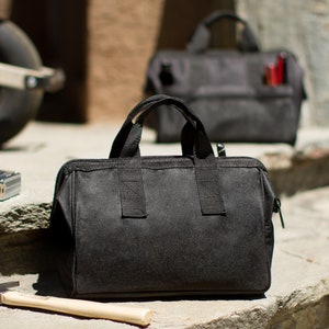 Puede incluir: Dos bolsas de herramientas de lona negra con cierres de cremallera y correas ajustables. La bolsa m&aacute;s peque&ntilde;a est&aacute; en el fondo y la bolsa m&aacute;s grande est&aacute; en primer plano.