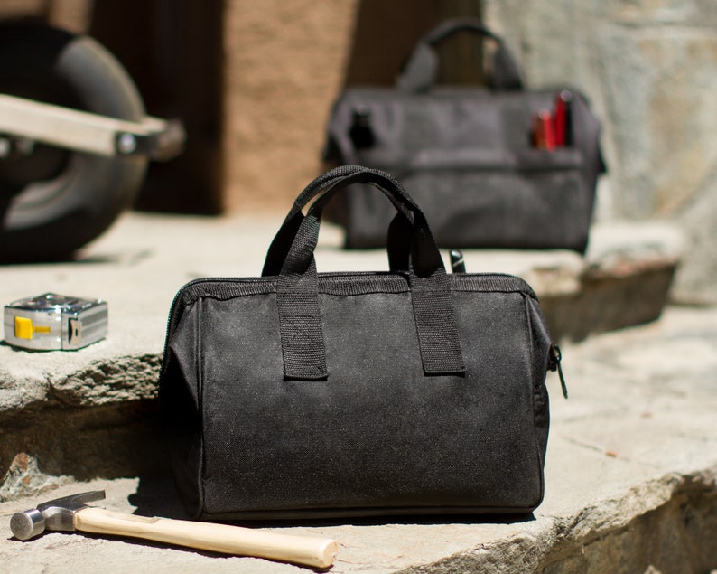 Puede incluir: Dos bolsas de herramientas de lona negra con cierres de cremallera y correas ajustables. La bolsa m&aacute;s peque&ntilde;a est&aacute; en el fondo y la bolsa m&aacute;s grande est&aacute; en primer plano.