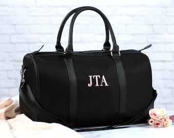 May include: Black duffel bag with leather accents and a pink embroidered monogram "JTA".