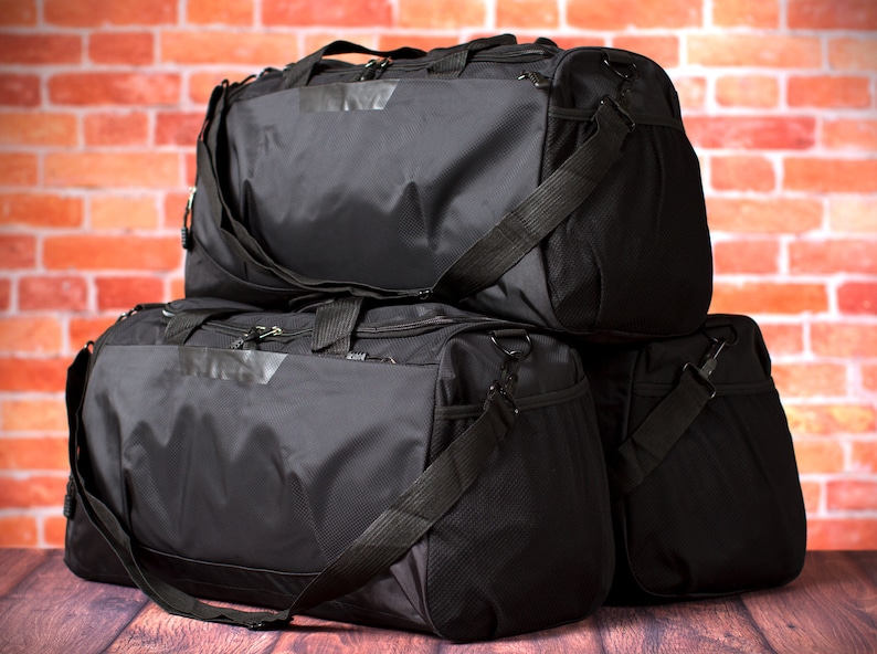 May include: Three black duffel bags stacked on top of each other. The bags have adjustable straps and zipper closures.