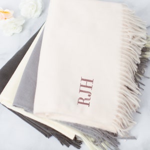 May include: A stack of four soft, fringed scarves in shades of gray, beige, and cream. The top scarf is personalized with the monogram "R.J.H."