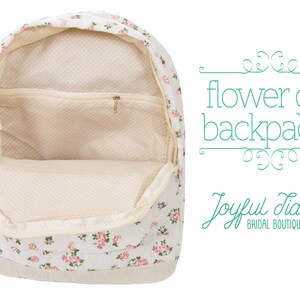 May include: A white canvas backpack with a floral print. The backpack has a zippered pocket on the front and a large main compartment. The backpack is open and the inside is lined with a cream-colored fabric. The text "flower girl backpacks" is written in green on a white background.
