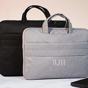 May include: Two laptop bags, one black and one gray. The gray bag has the initials "R.J.H." embroidered on the front in pink thread.