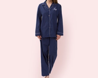 May include: Navy blue pajama set with white piping trim. The long-sleeved top has a button-down front and the name "Amy" embroidered in white script. The matching pants are wide-legged.