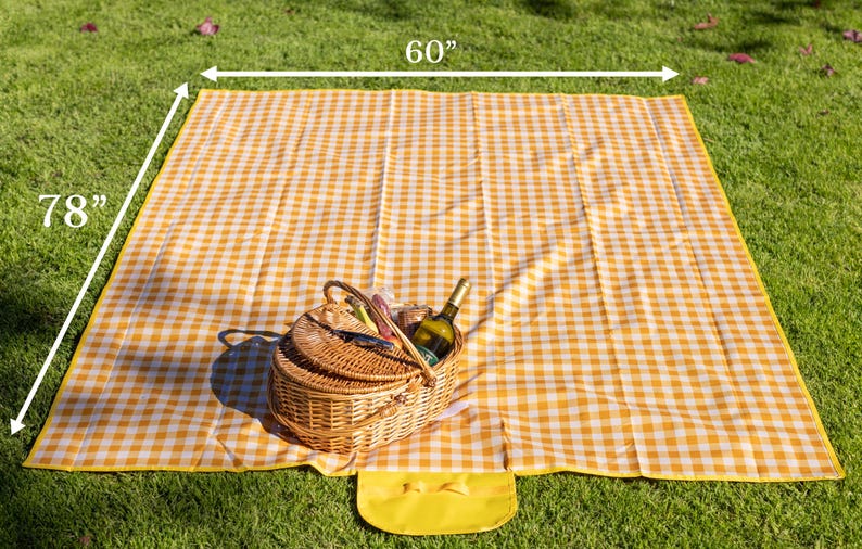 Puede incluir: Una manta de picnic a cuadros amarillos y blancos, de 152 x 198 cm, est&aacute; extendida sobre hierba verde. Una cesta de picnic de mimbre con una botella de vino y otros art&iacute;culos est&aacute; sobre la manta. Una peque&ntilde;a bolsa amarilla est&aacute; adjunta.