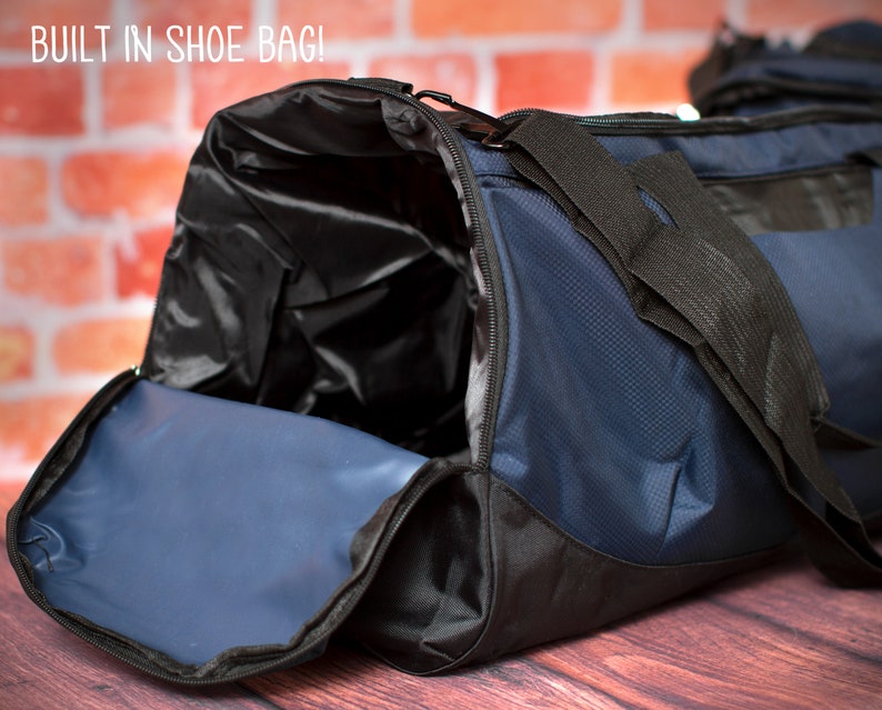 May include: A blue and black duffel bag with a built-in shoe bag. The bag is open and the shoe bag is visible. The bag is sitting on a wooden surface.