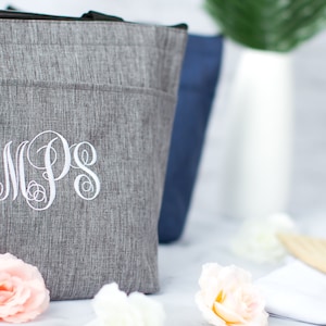 May include: A gray insulated tote bag with a white monogram "MPS" embroidered on the front. The bag is sitting on a white surface with white and pink flowers.