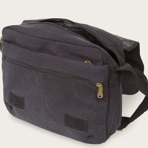 May include: A black canvas messenger bag with a zippered pocket and two velcro closures. The bag has a long adjustable strap.