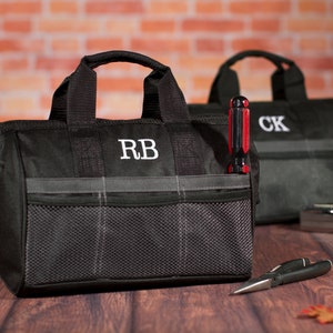 May include: Two black canvas tool bags with gray accents and zipper closures. The bags have mesh pockets and are personalized with the initials "RB" and "CK".