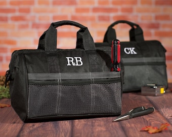 May include: Two black canvas tool bags with gray accents and zipper closures. The bags have mesh pockets and are personalized with the initials "RB" and "CK".