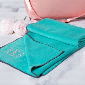 May include: A turquoise microfiber yoga towel with a gray border and the monogram "KTB" embroidered in pink.