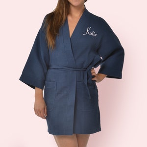 May include: A navy blue waffle weave robe with a white embroidered name "Kallie" on the left side of the chest.