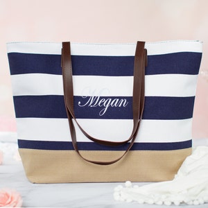 Puede incluir: Una bolsa de lona de rayas blancas y azul marino con asas de cuero marr&oacute;n. La bolsa tiene un fondo beige y el nombre "Megan" est&aacute; bordado en la parte delantera.