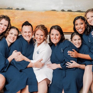May include: A group of individuals wearing matching navy blue waffle-knit robes, with one individual in the center wearing a white waffle-knit robe. Each robe features a long-sleeve design with a tie-waist closure and a textured waffle pattern.