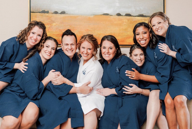 May include: A group of individuals wearing matching navy blue waffle-knit robes, with one individual in the center wearing a white waffle-knit robe. Each robe features a long-sleeve design with a tie-waist closure and a textured waffle pattern.