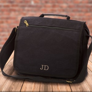 May include: A black canvas messenger bag with a zippered closure and a top handle. The bag has a personalized monogram "JD" on the front.