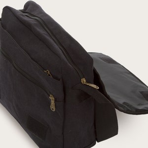 May include: A black canvas messenger bag with a zippered flap and a smaller zippered pocket on the front. The bag has a long adjustable strap and a velcro closure.