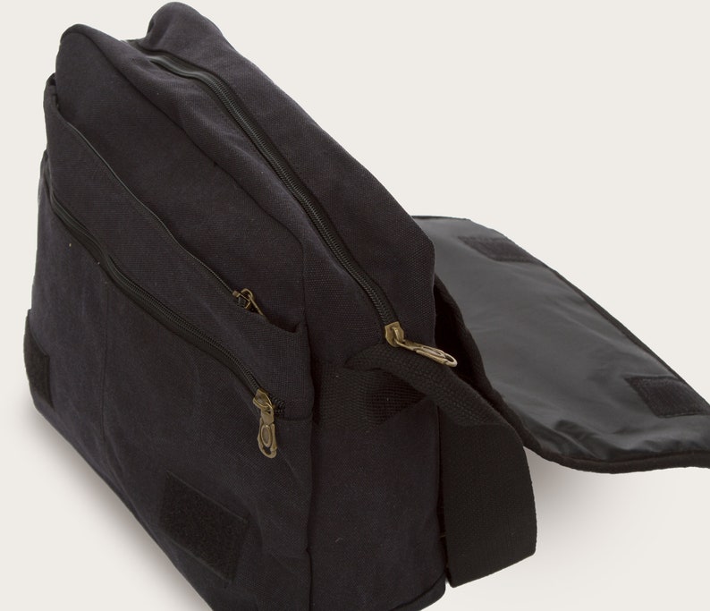 May include: A black canvas messenger bag with a zippered flap and a smaller zippered pocket on the front. The bag has a long adjustable strap and a velcro closure.