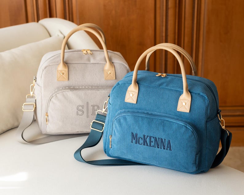 May include: Two corduroy bags with tan handles and straps. One is light gray with the initials "SP" embroidered on the front. The other is blue with the name "McKenna" embroidered on the front. Both have gold zippers.