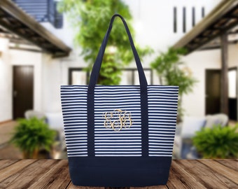 May include: A blue and white striped canvas tote bag with a navy blue bottom. The bag has two navy blue handles and a gold monogram in the center.
