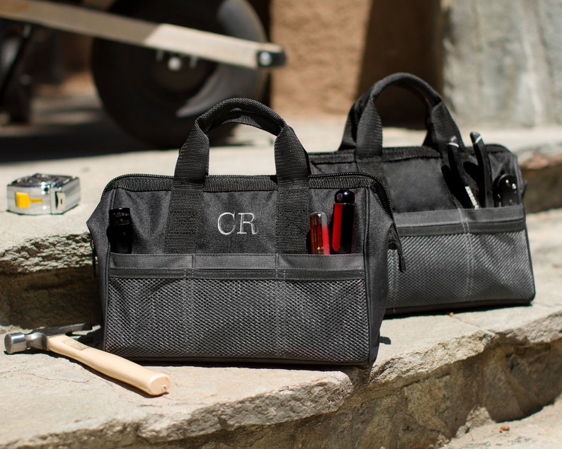 Puede incluir: Dos bolsas de herramientas de lona negra con m&uacute;ltiples bolsillos y un compartimento de malla. La bolsa de la izquierda tiene las iniciales "CR" bordadas en la parte delantera.