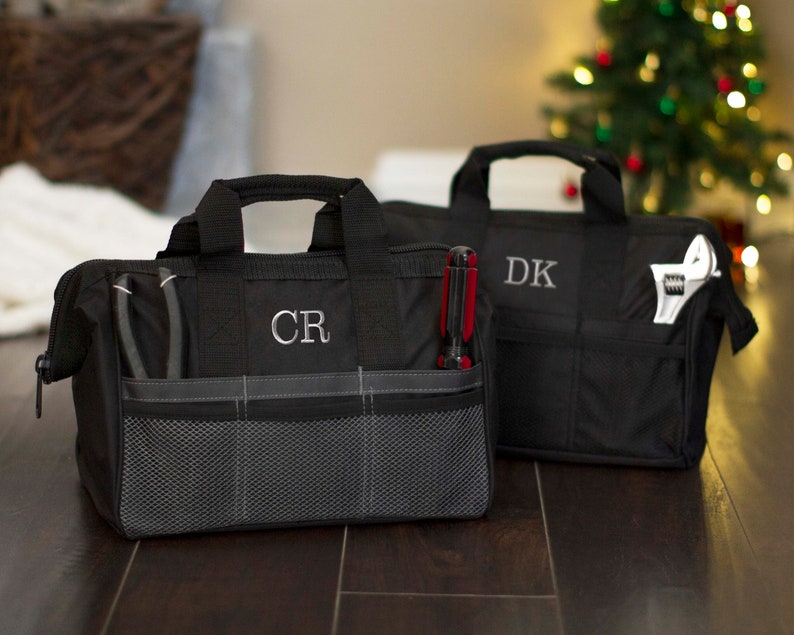 K&ouml;nnte beinhalten: Zwei schwarze Werkzeugtaschen mit mehreren Taschen und einem Rei&szlig;verschluss. Die Tasche links hat die Initialen "CR" auf der Vorderseite gestickt. Die Tasche rechts hat die Initialen "DK" auf der Vorderseite gestickt.
