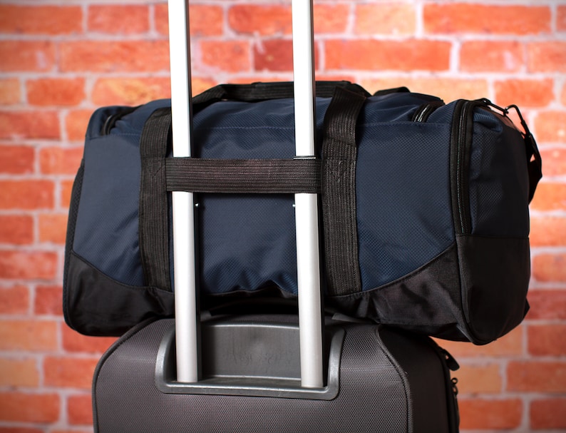 K&ouml;nnte beinhalten: Ein schwarzer Rollkoffer mit einer dunkelblauen Reisetasche oben drauf. Die Reisetasche hat zwei Riemen und einen Rei&szlig;verschluss.