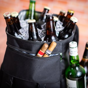 K&ouml;nnte beinhalten: Eine schwarze isolierte K&uuml;hltasche mit einer Rei&szlig;verschlusstasche. Die Tasche ist gef&uuml;llt mit braunen Glasflaschen und Eis. Zwei braune Zigarren ragen aus der Tasche.